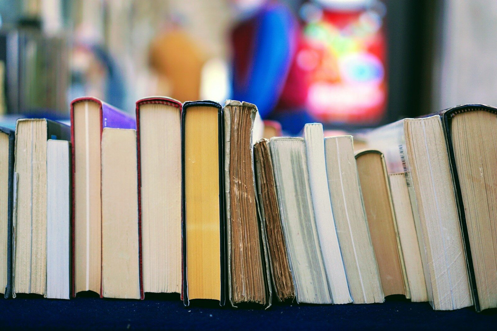 Row of varied books with worn and pristine spines, displayed on a table, suggesting a vibrant book market or sale atmosphere.
